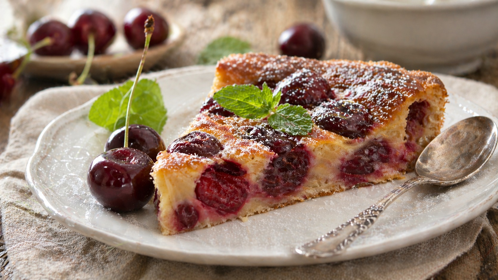 Part de clafoutis aux cerises dorée avec sucre glace dans une assiette blanche